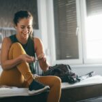 woman in athletic wear tying her shoes while sitting at the edge of the bed. Getting ready to work out.