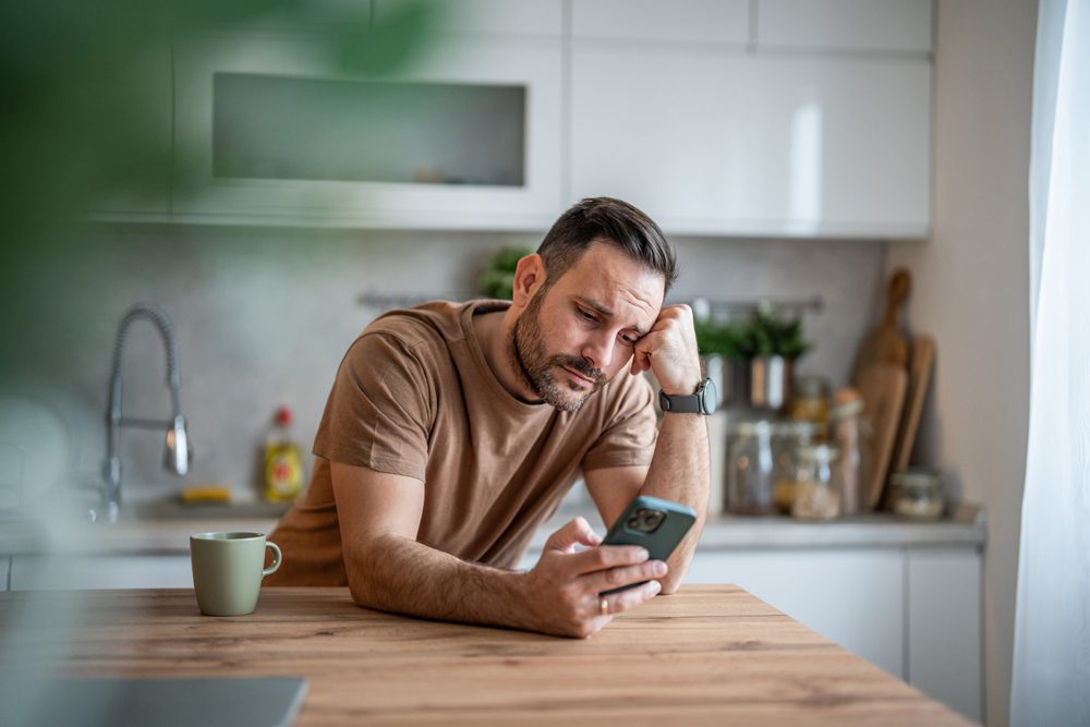 man leaning on the kitchen counter doomscrolling on his phone
