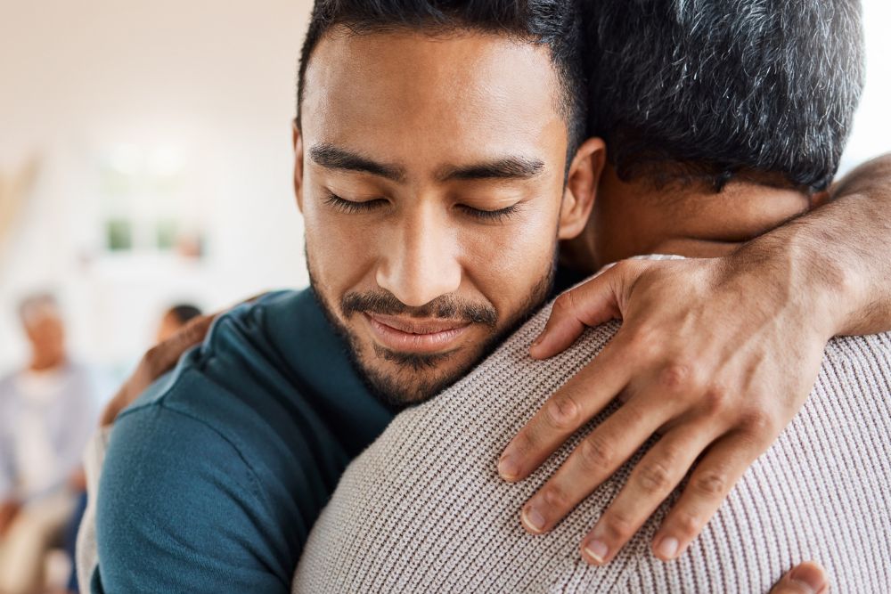 Two men warmly hugging, one with eyes closed and a peaceful expression
