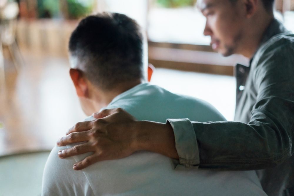 Man offering support by placing a comforting hand on another man's back, symbolizing empathy, compassion, and emotional support during a difficult time.