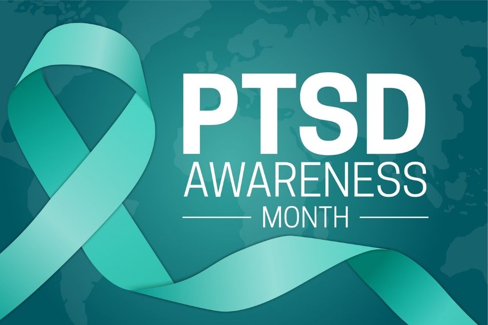 Teal awareness ribbon on a dark teal background with the text "PTSD Awareness Month" in bold white letters. The ribbon symbolizes support for PTSD awareness.
