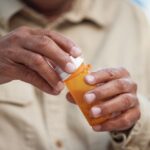 Close-up of a person’s hands opening a prescription pill bottle, symbolizing medication use in recovery and mental health treatment.