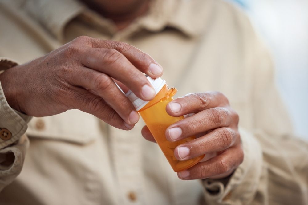 Close-up of a person’s hands opening a prescription pill bottle, symbolizing medication use in recovery and mental health treatment.