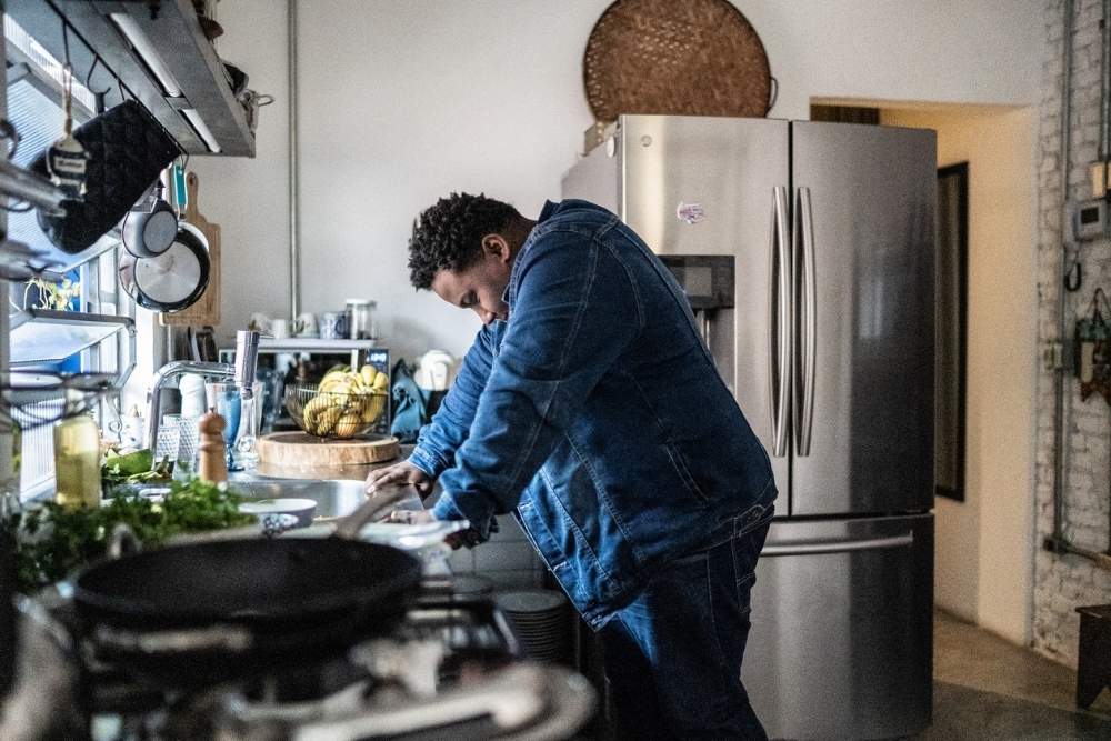 A person leaning over a kitchen counter with their head down, appearing overwhelmed or distressed, in a modern home setting.