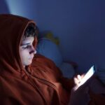 Teenager using a smartphone lying in bed late at night, playing games, watching videos online, and scrolling the screen