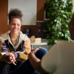A woman smiling while seated and talking with another person in a calm, indoor counseling setting.