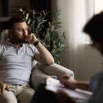 Miramount - Genetics and Dual Mental Health Diagnoses. A young man sits in a therapy session in a private office. He looks out the window in a daze while a therapist writes notes.